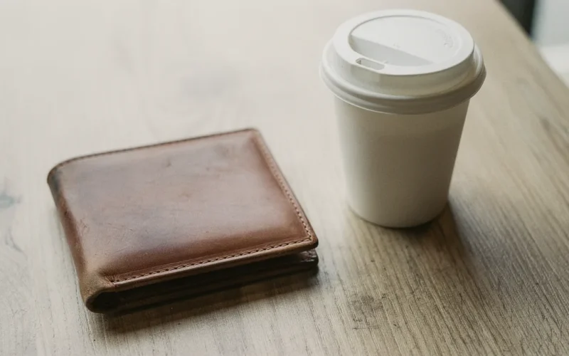 Kafe masasında kapalı kahverengi deri cüzdan ve baskısız karton bardak